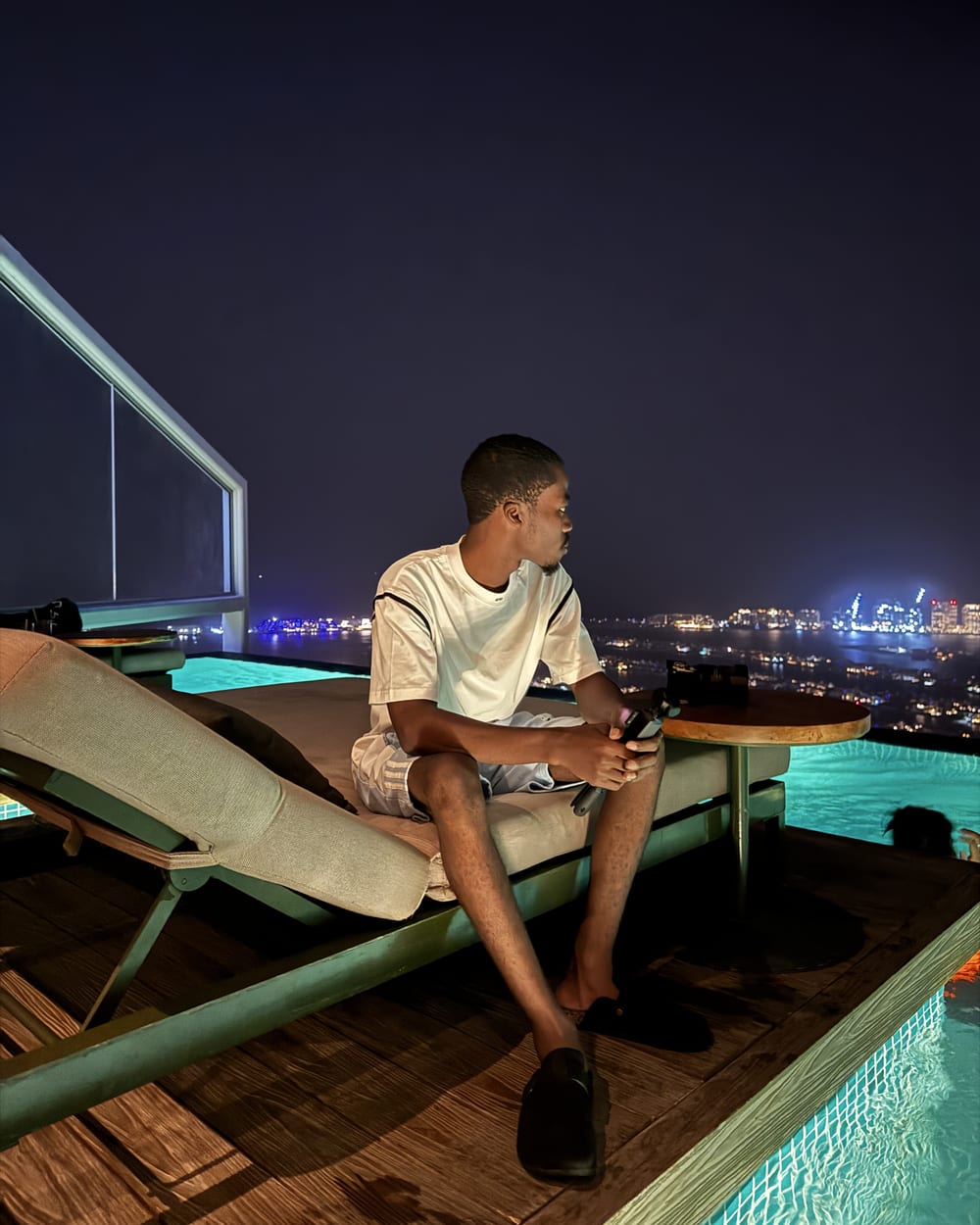 Chancio seul le soir sur un rooftop de Dubaï, caméra à la main, face aux lumières de la ville